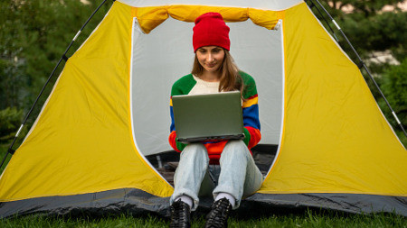 Junge Frau arbeitet an einem Laptop. Sie sitzt in einem Campingzelt.