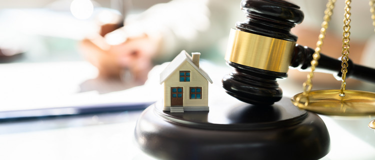 Ein Mini-Modell eines Hauses auf einem Klopfblock neben einem Richterhammer 