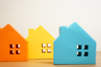 ein Bild von drei Häusern aus Pappe, links orange, mittig gelb und rechts blau