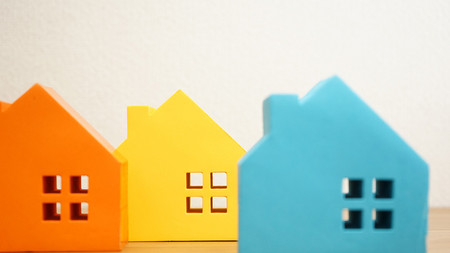 ein Bild von drei Häusern aus Pappe, links orange, mittig gelb und rechts blau